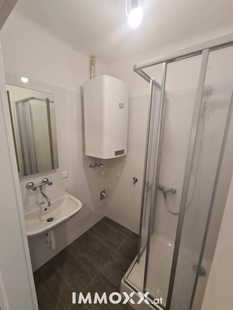 Helles Badezimmer mit Duschkabine, Waschbecken, Spiegel und praktischem Handtuchheizkörper.