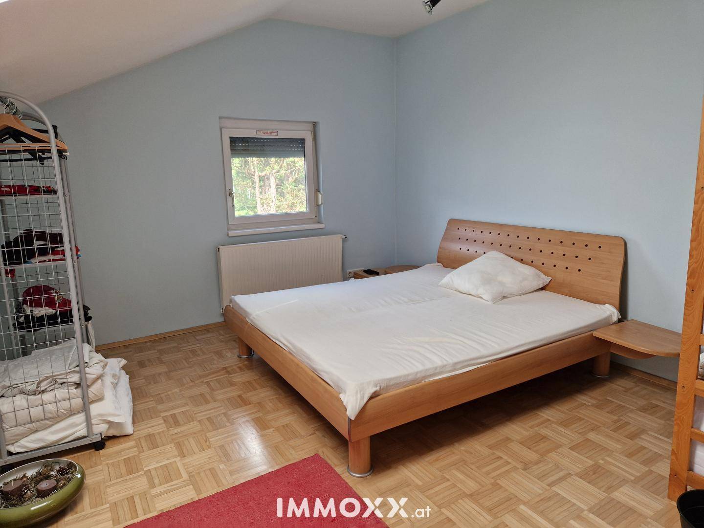 Schlafzimmer mit hellblauen Wänden, Holzbett und Parkettboden unter einer Dachschräge.