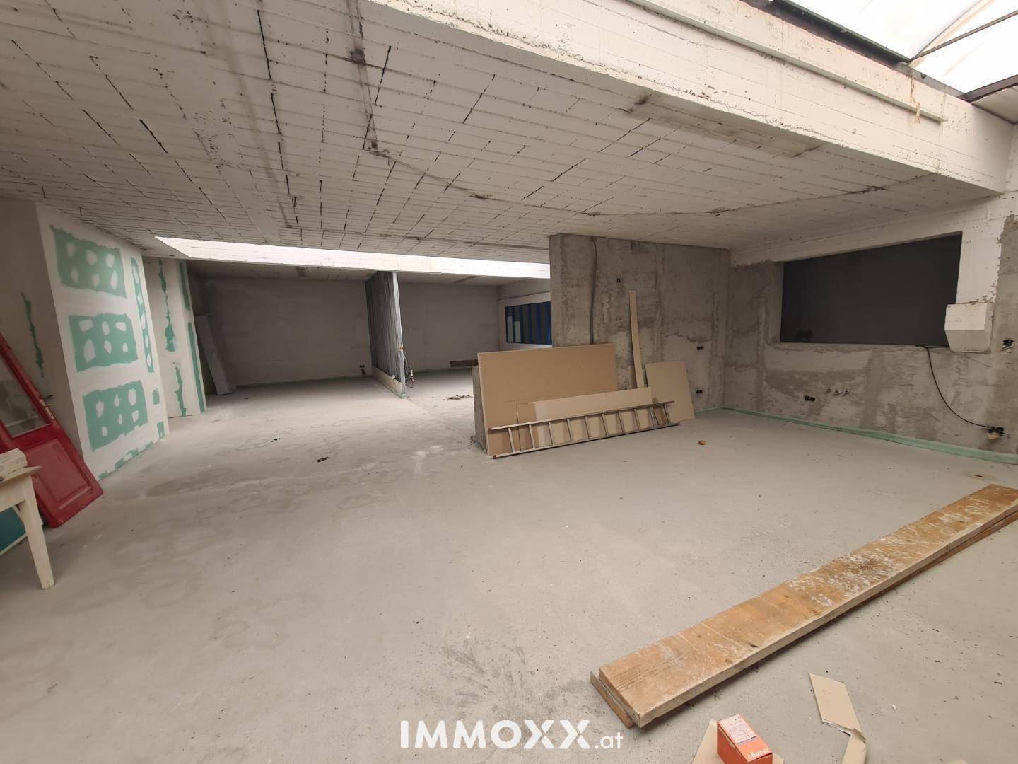 Unfertiger Innenraum im Rohbau mit Betonwänden und großem Dachfenster, bereit für den Ausbau.