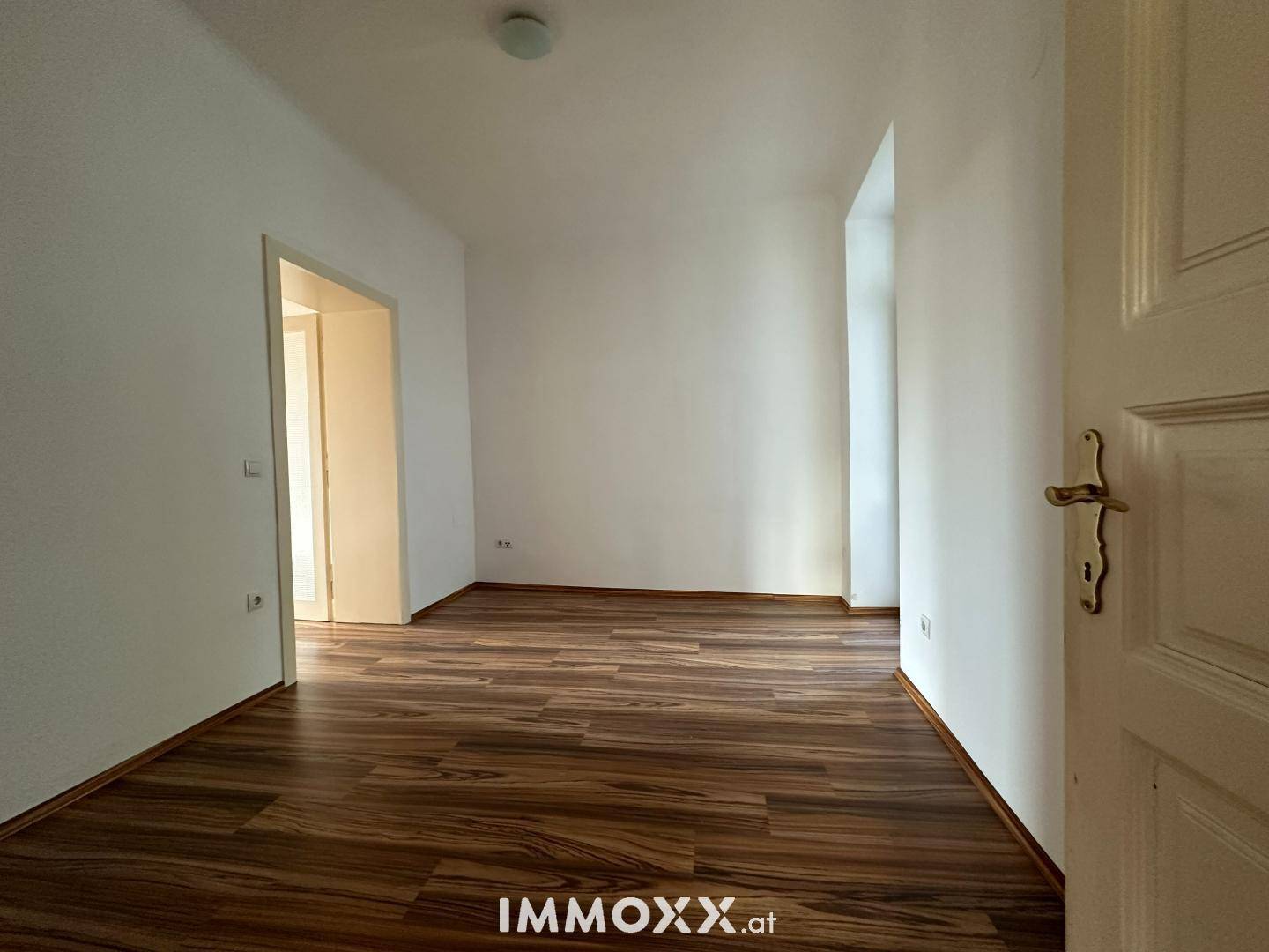 Leerer Raum mit Laminatboden und einer offenen Tür zu einem weiteren Zimmer.
