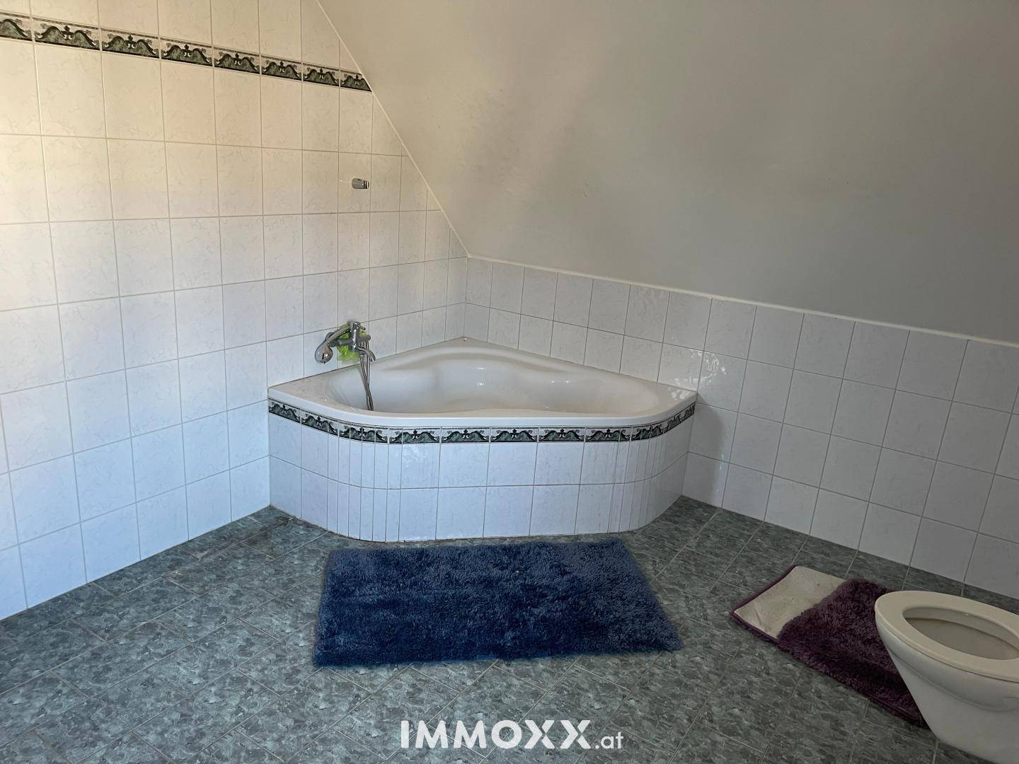 Badezimmer mit Eckbadewanne, weißen Fliesen und Dachschräge, bereit zur Modernisierung.