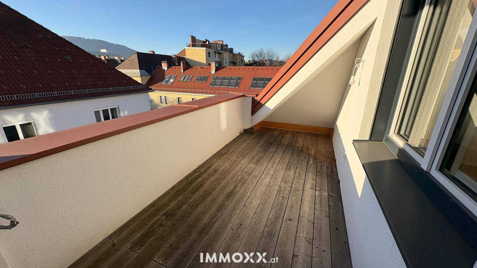 Geräumige Dachterrasse mit Holzboden und Blick über die umliegenden Dächer der Stadt.