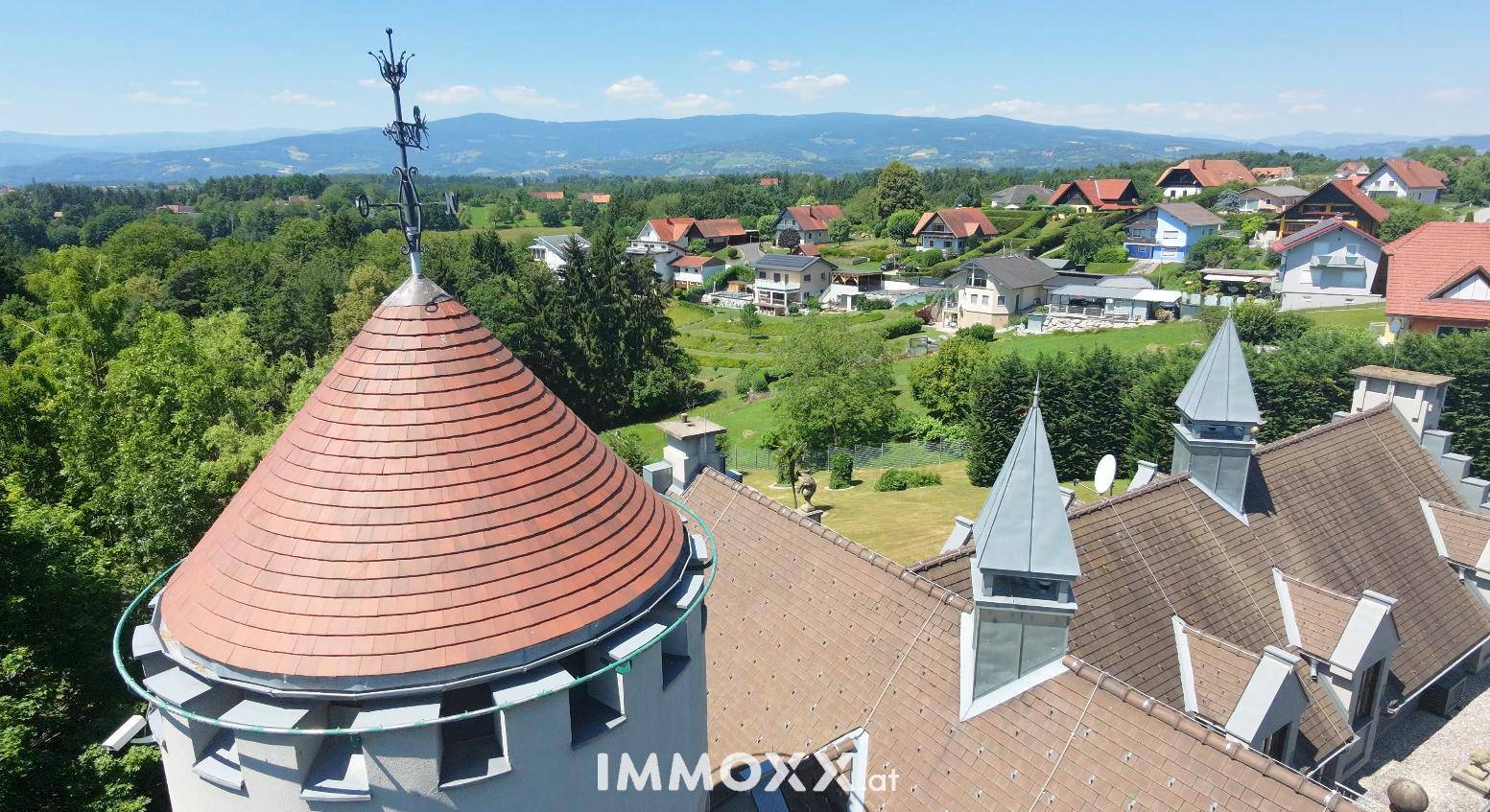 Detailansicht des Schlossturms und Daches mit weitem Blick über die grüne Landschaft und Berge.