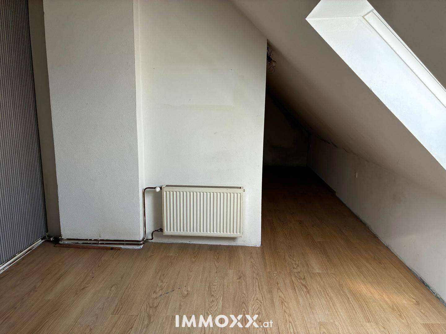 Dachgeschosszimmer mit Laminatboden, schrägen Wänden und einem Dachfenster.