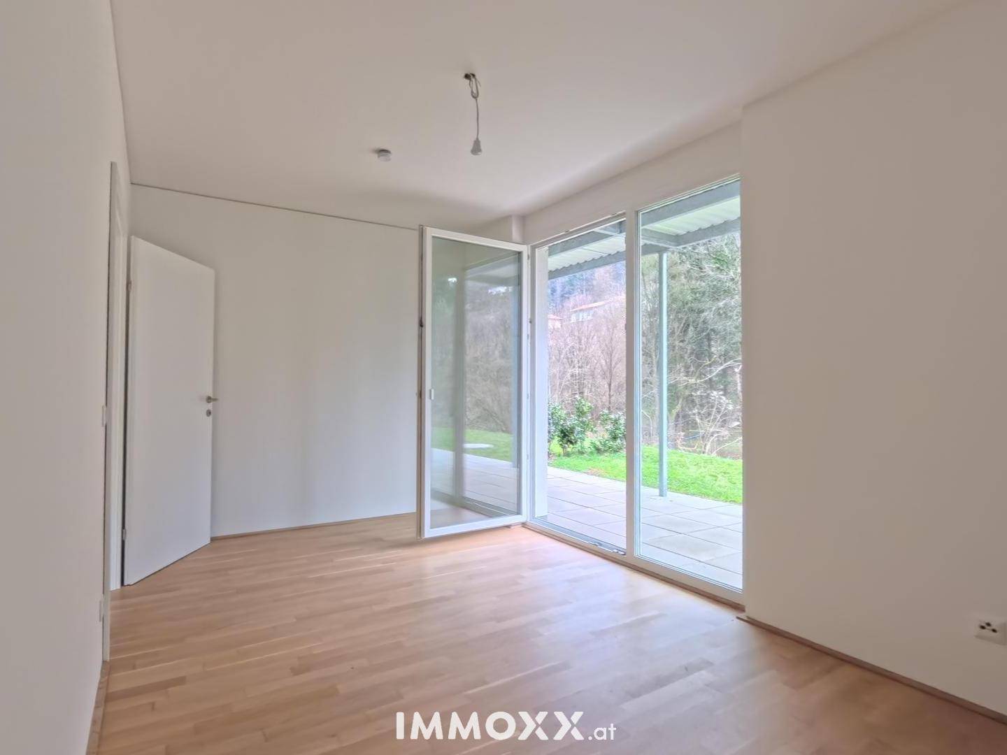 Heller Raum mit Holzboden und großen Glastüren, die Zugang zu einer Terrasse bieten.