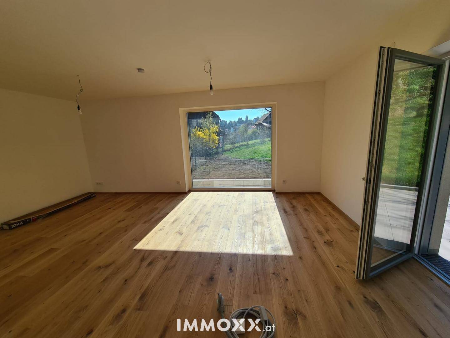 Lichtdurchfluteter Wohnraum mit breiten Holzplanken und weitem Blick ins Grüne.