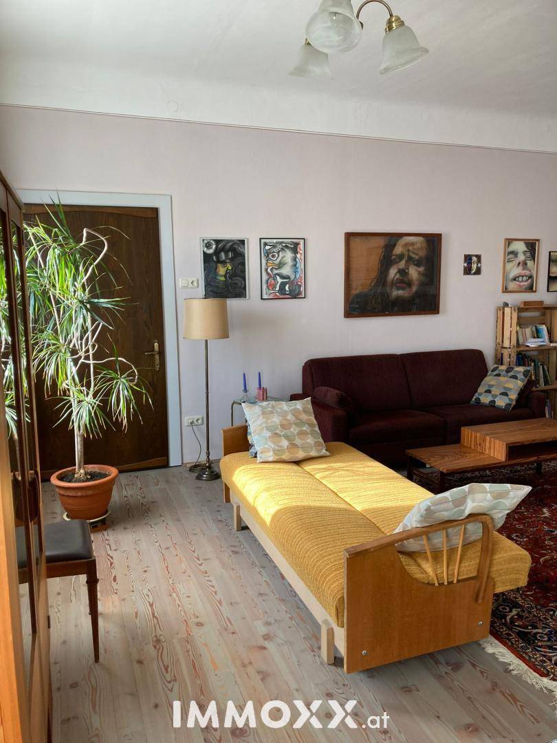 Gemütliches Wohnzimmer mit Holzboden, Sofa und dekorativen Bildern an der Wand.