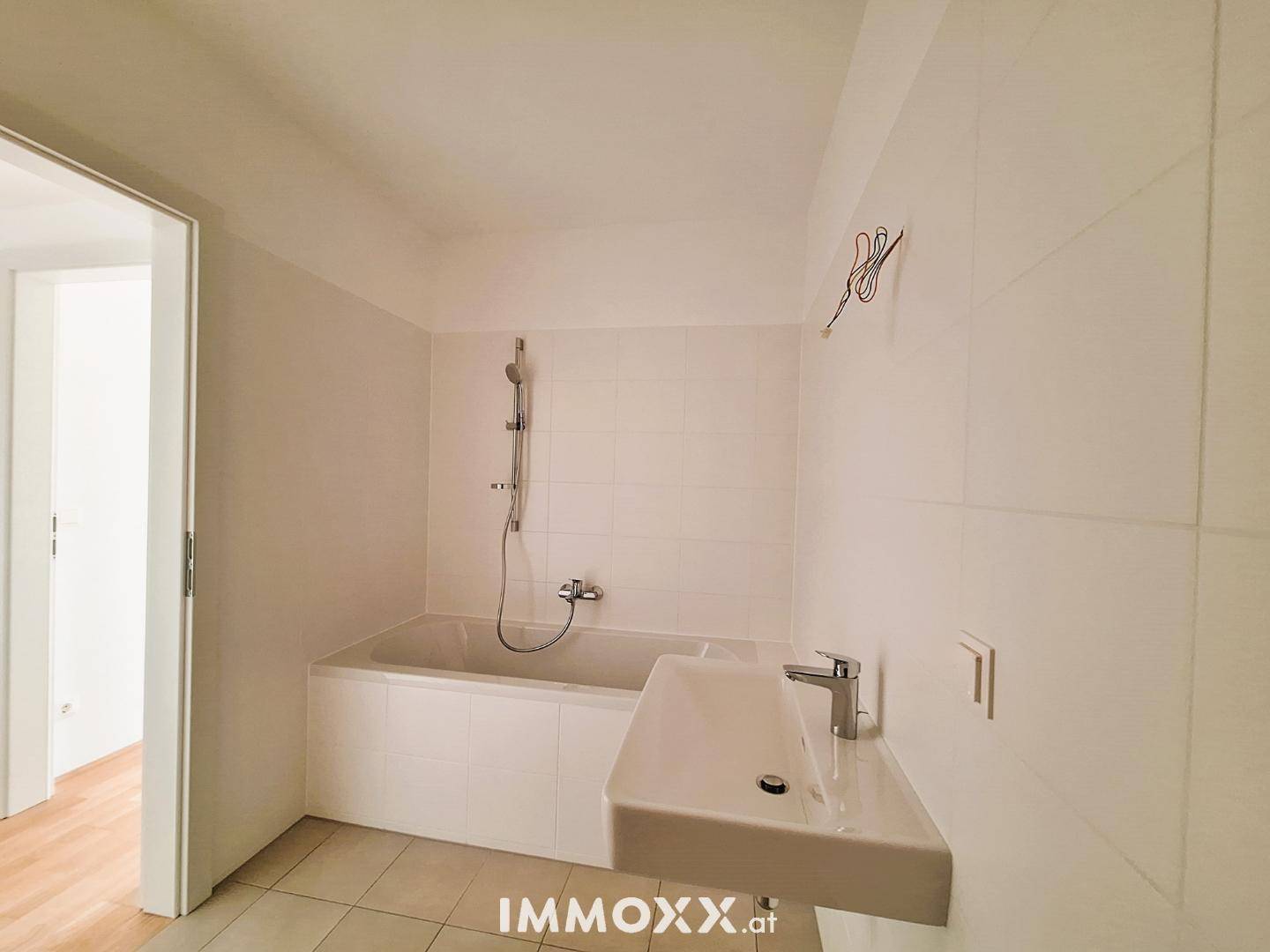 Sauber gefliestes Badezimmer mit Badewanne und modernem Waschbecken, bereit zum Einzug.