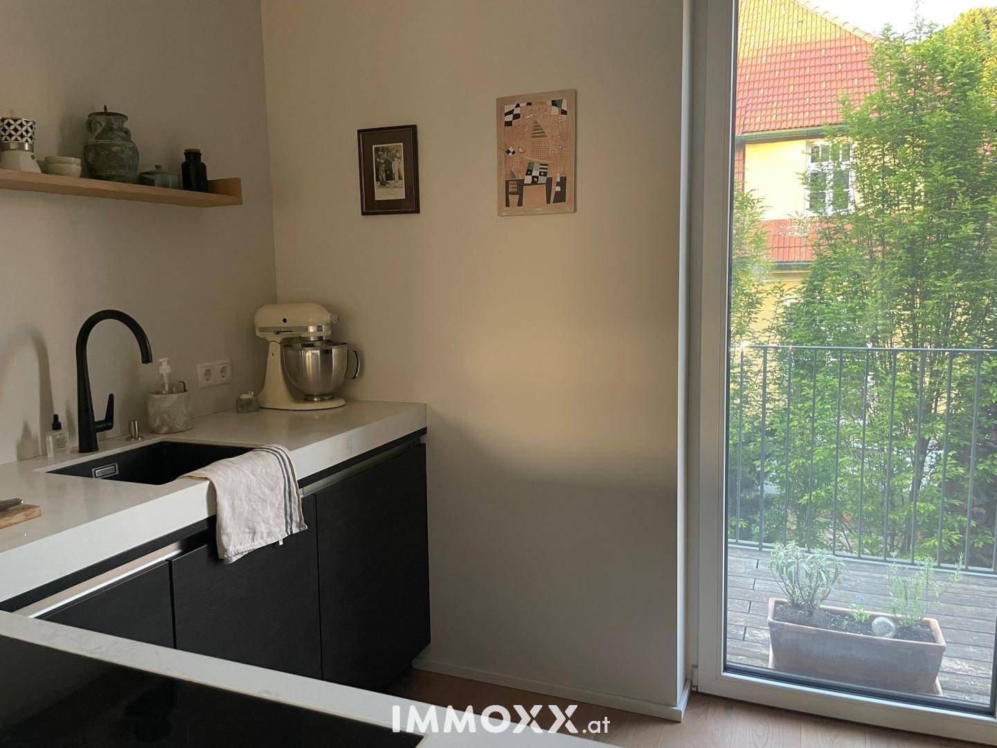 Kompakte Küchenzeile mit schwarzer Spüle, weißer Arbeitsplatte und Induktionskochfeld, mit Zugang nach draußen.