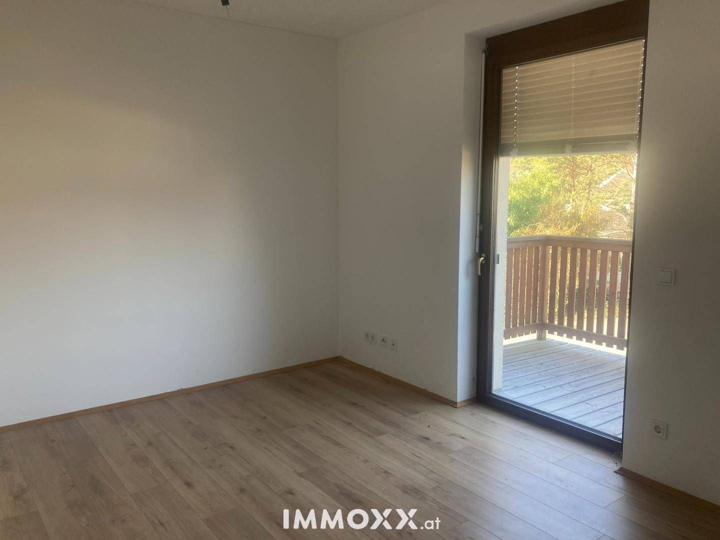 Heller Raum mit Laminatboden und Zugang zu einem Balkon, der viel Licht spendet.