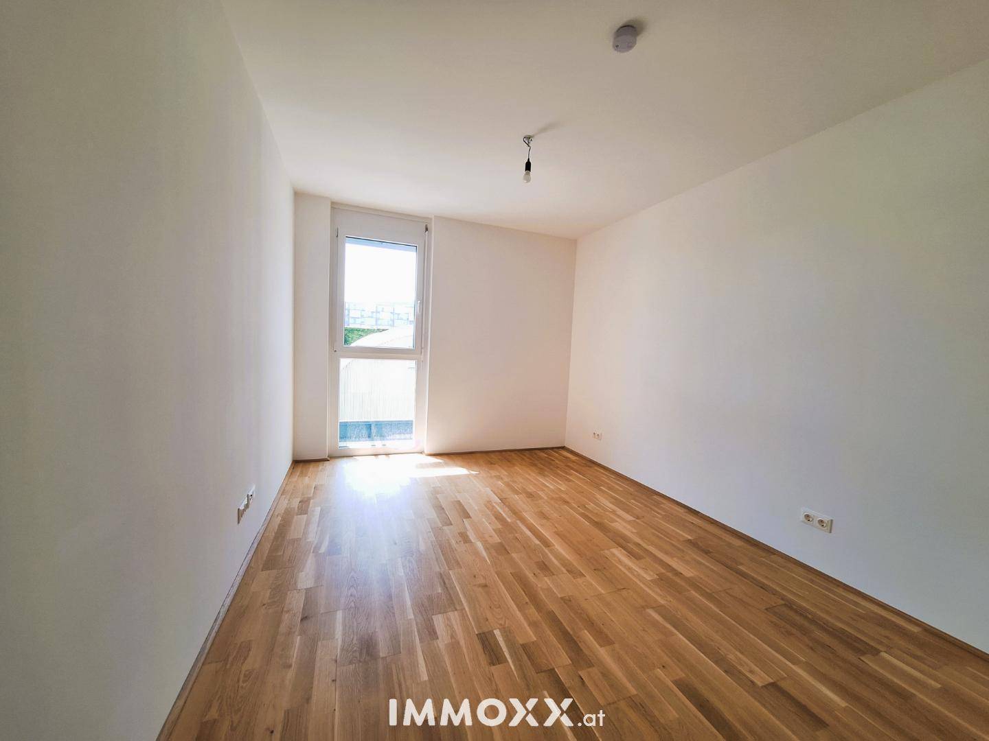 Helles Schlafzimmer mit Holzboden und Fenster, das einen Ausblick bietet.