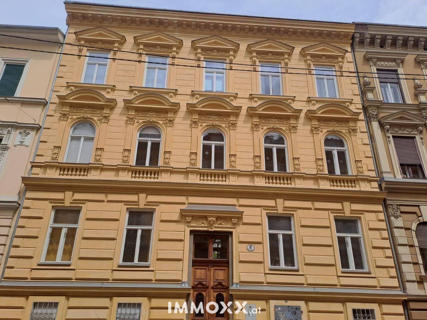 Historische Fassade eines Altbaus mit reich verzierten Fenstern und einem imposanten Eingangsbereich.