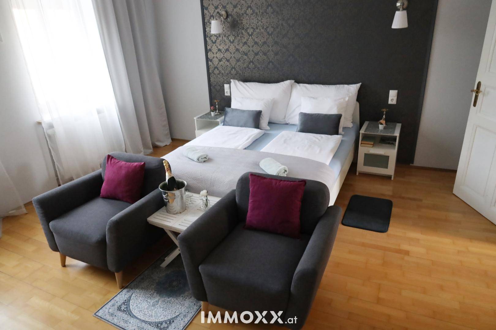 Gemütliches Schlafzimmer mit Doppelbett, zwei Sesseln und dunkler Akzentwand.