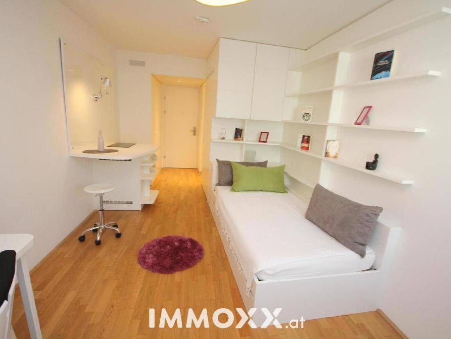 Modernes Studio-Apartment mit hellem Holzboden, integriertem Bett und funktionalem Schreibtischbereich.