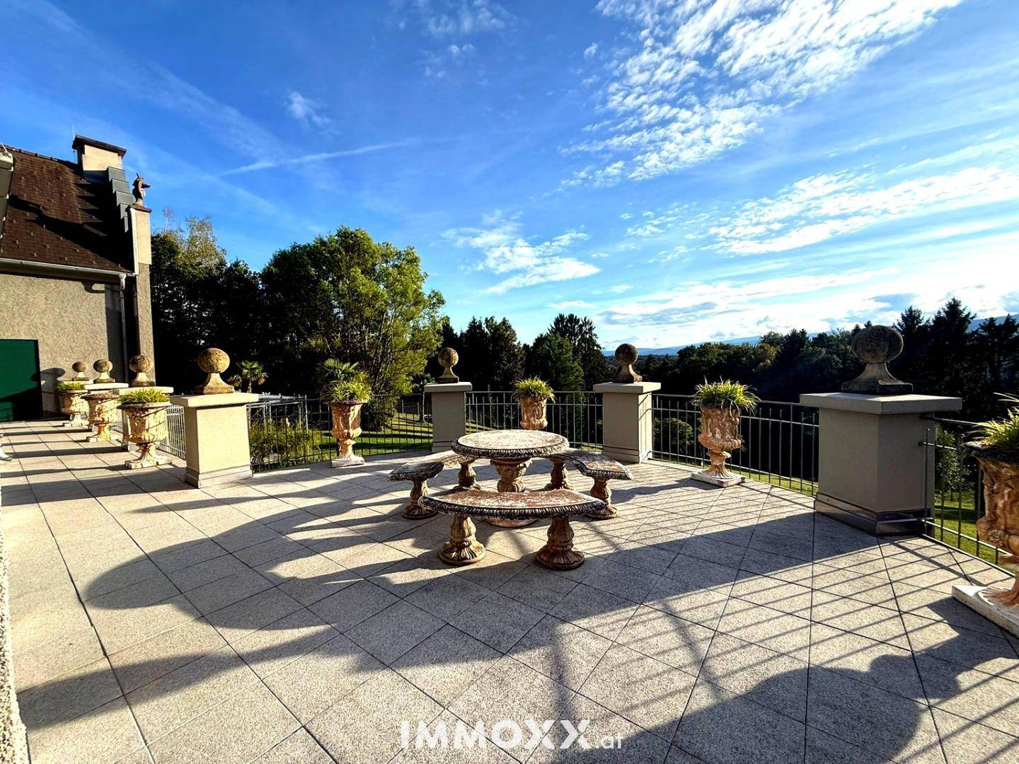 Große gepflasterte Terrasse mit Steingarnitur und weitem Blick ins Grüne unter blauem Himmel.