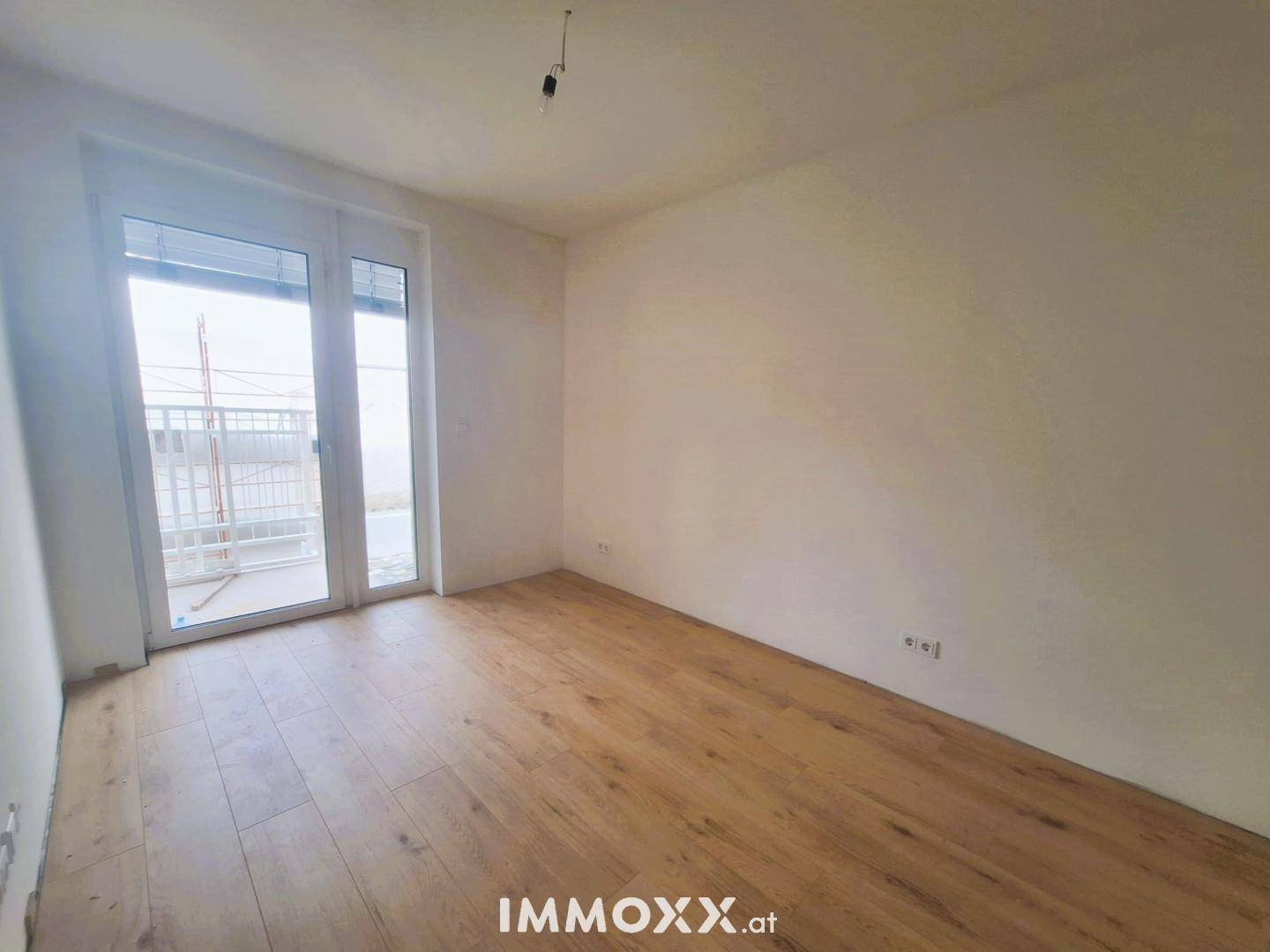 Helles Zimmer mit Holzboden und Zugang zu einem Balkon oder einer Terrasse.