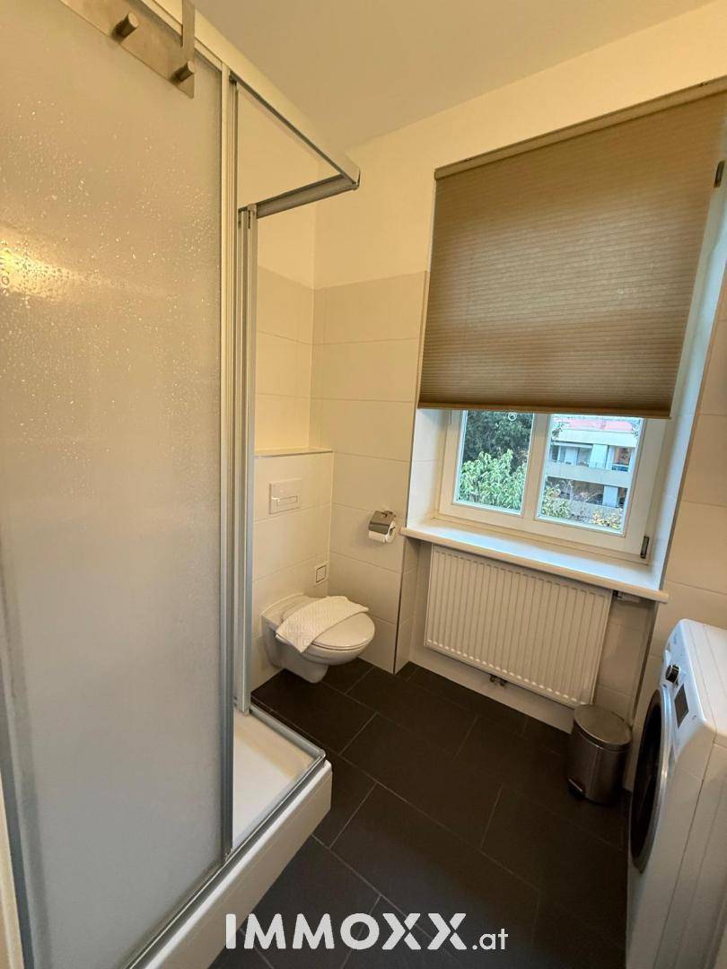 Funktionales Badezimmer mit Duschkabine, WC und Waschmaschine, ausgestattet mit Fenster.