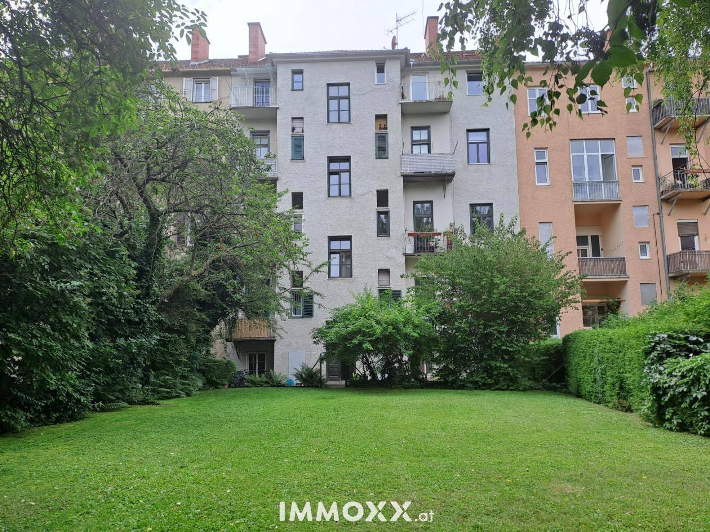 Großer, gepflegter Gemeinschaftsgarten mit weitläufiger Rasenfläche und altem Baumbestand hinter dem Gebäude.