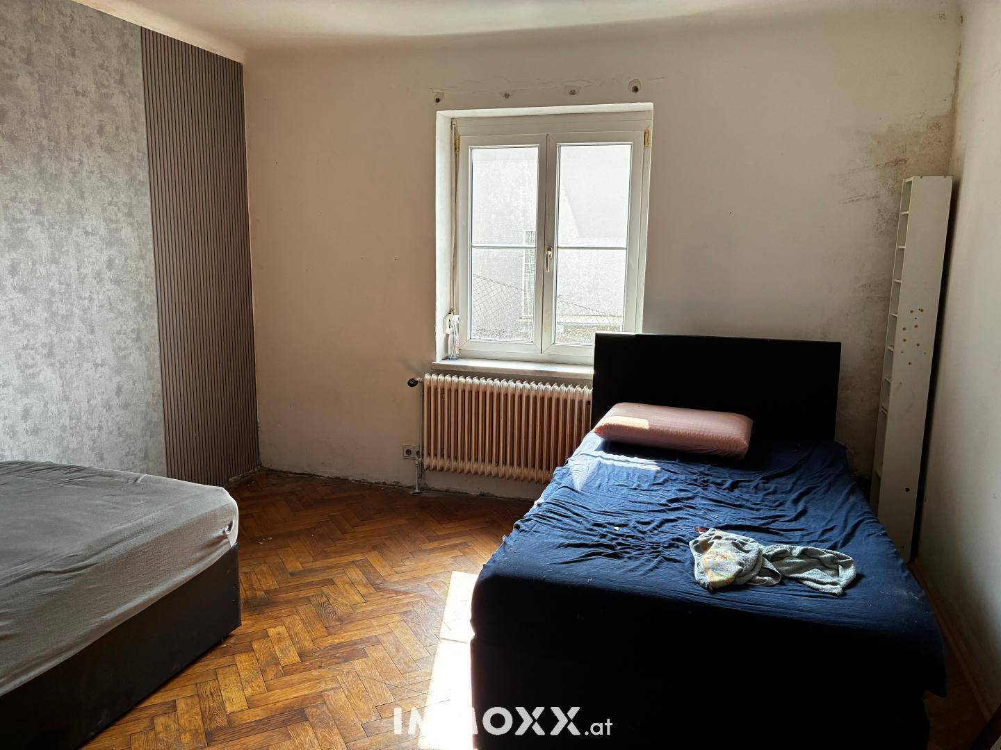Schlafzimmer mit Fischgrätparkett, zwei Betten und einem Fenster.
