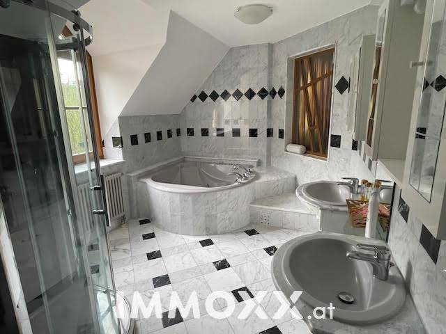 Luxuriöses Badezimmer mit Marmorfliesen, Doppelwaschbecken, Eckbadewanne und separater Dusche.