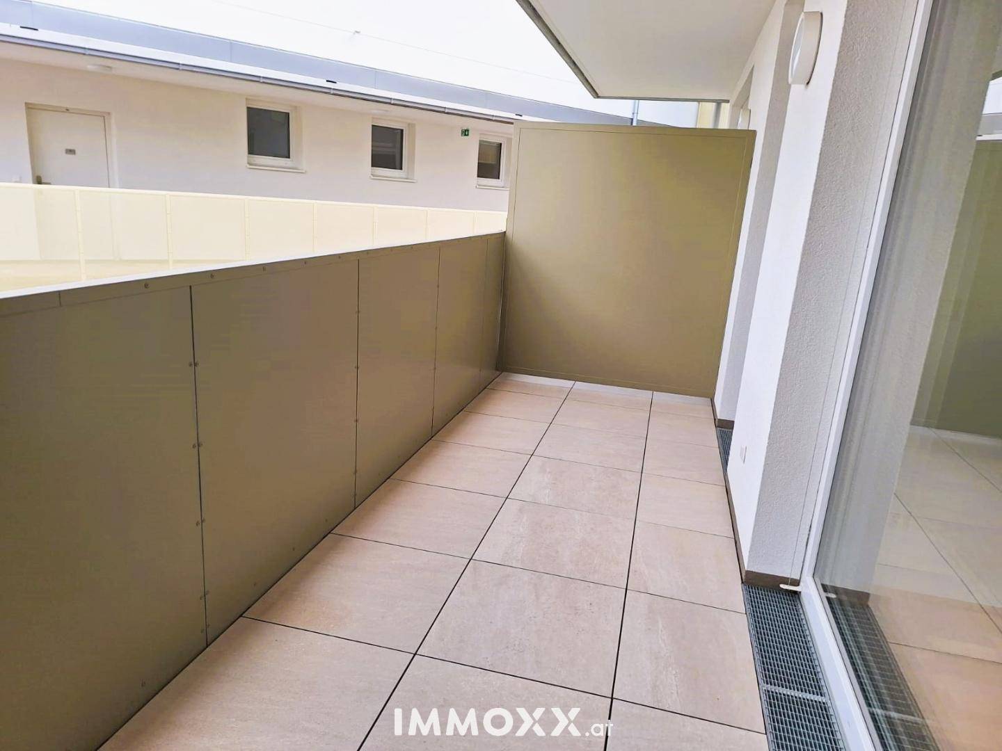 Heller Balkon mit Fliesenboden und Blick auf den Innenhof, ideal für Entspannung im Freien.