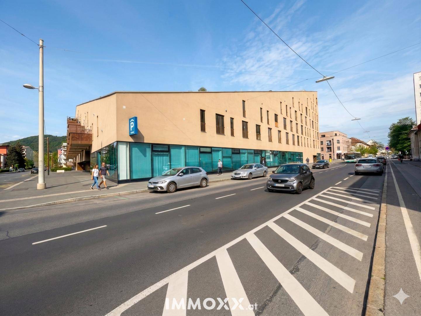 Ansicht des modernen Gebäudes von einer anderen Straßenseite, mit Parkplatzschild und vorbeifahrenden Autos.