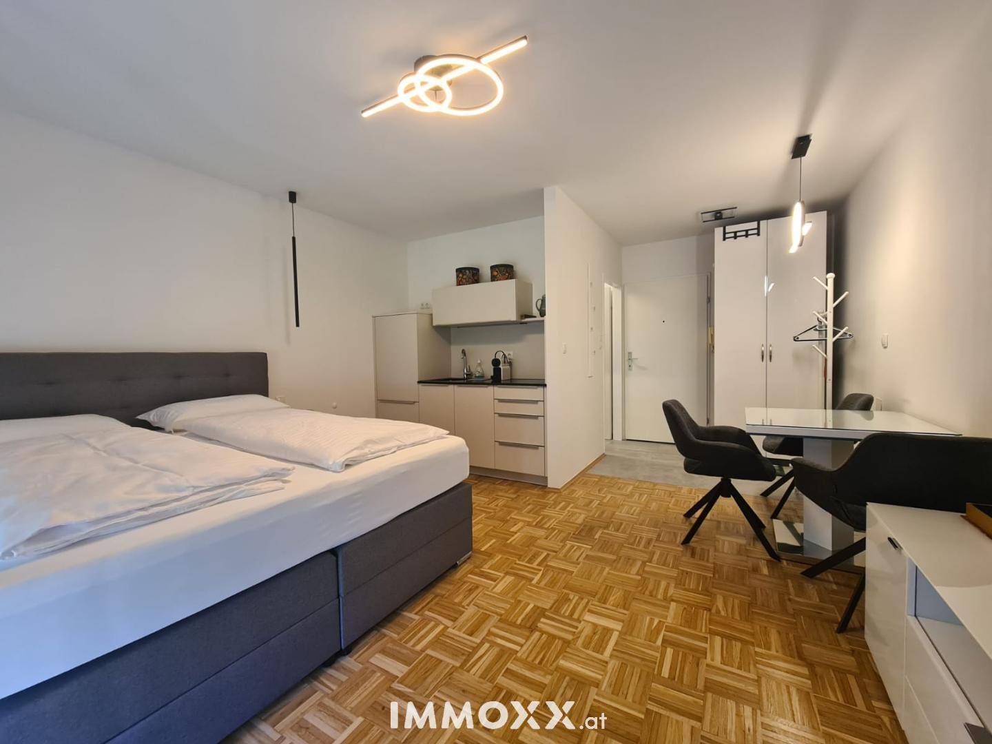 Helles Studio-Apartment mit Schlafbereich, kleiner Küchenzeile und Essbereich auf Parkettboden.