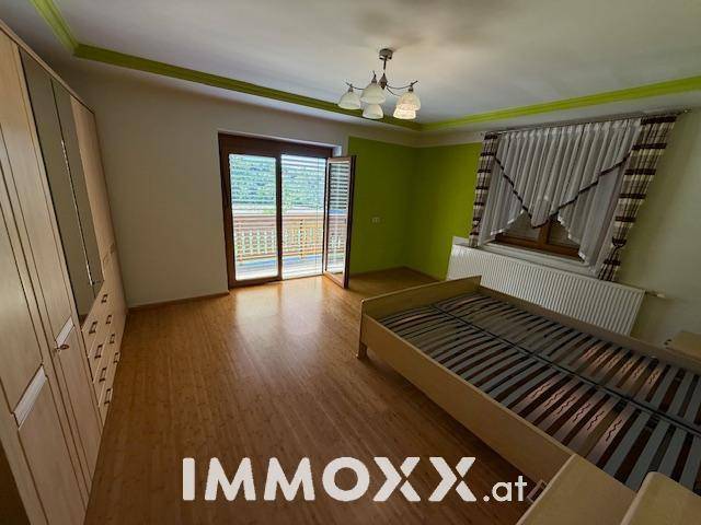 Schlafzimmer mit Holzboden, grüner Akzentwand und Zugang zu einem Balkon mit Bergblick.