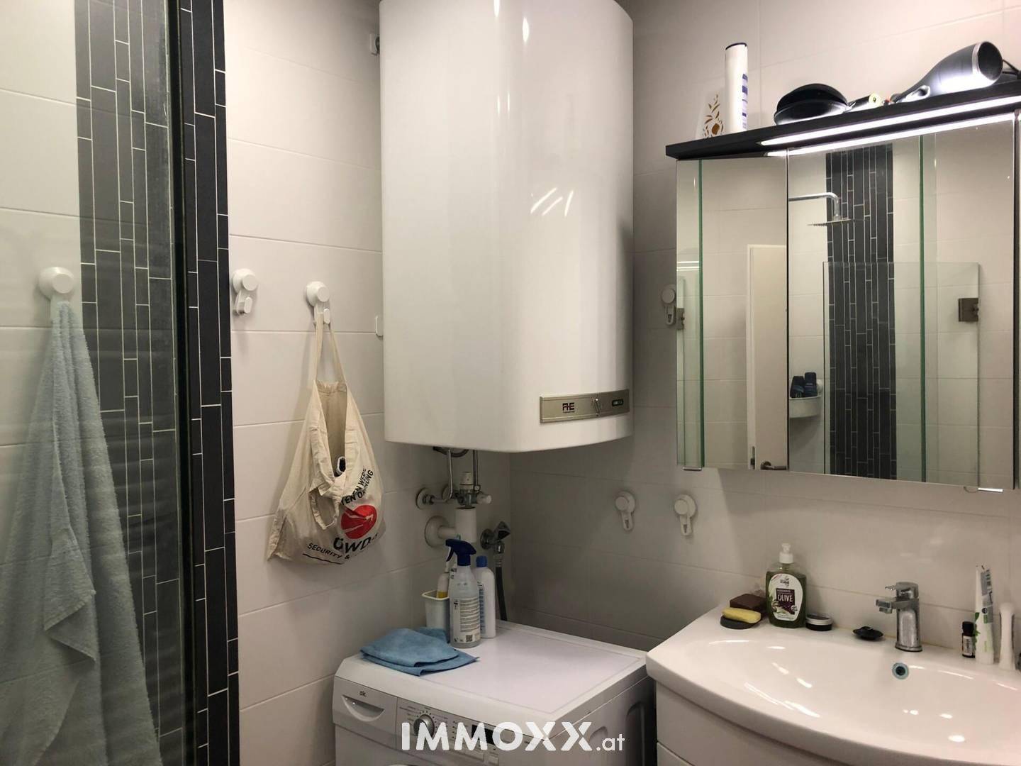 Modern gefliestes Badezimmer mit Dusche, Waschbecken und Warmwasserboiler.