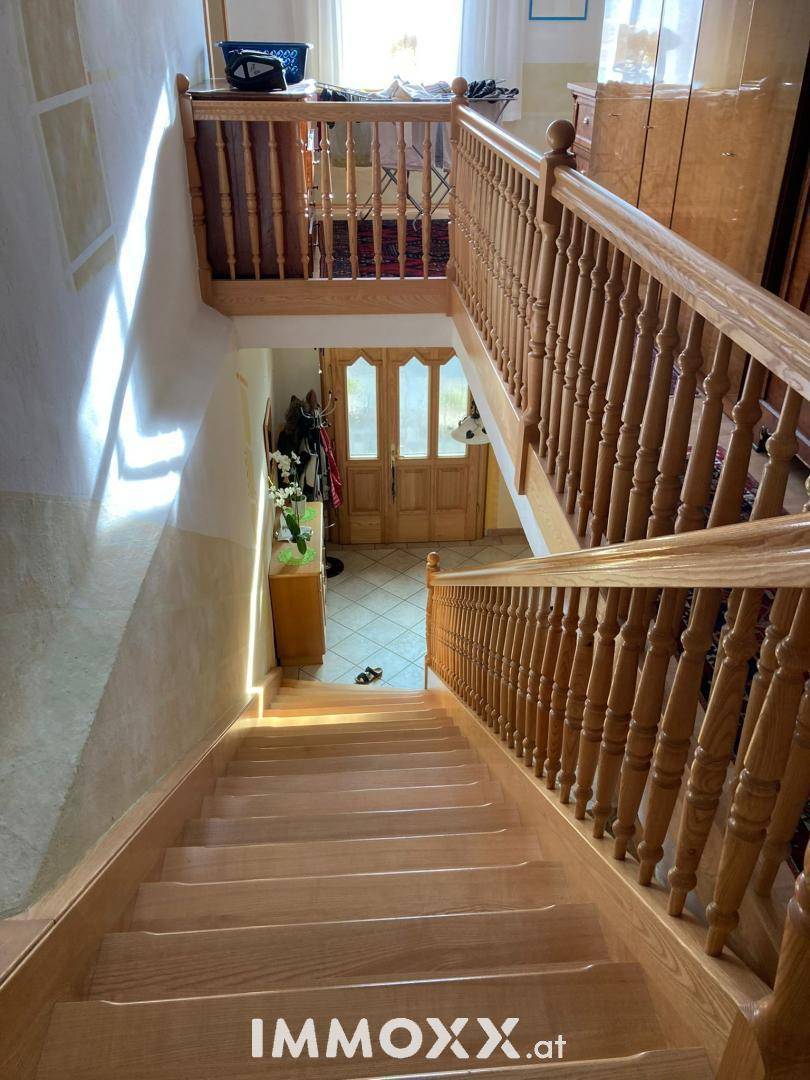 Helles Treppenhaus mit Holztreppe und Holzgeländer, das zum Eingangsbereich führt.