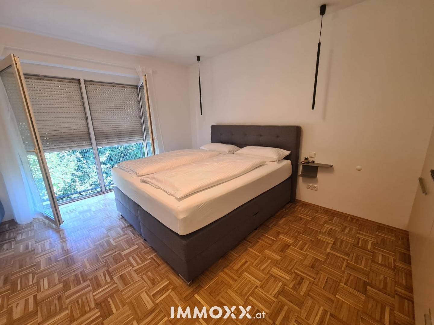 Gemütliches Schlafzimmer mit großem Doppelbett und Zugang zu einem Balkon mit grüner Aussicht.