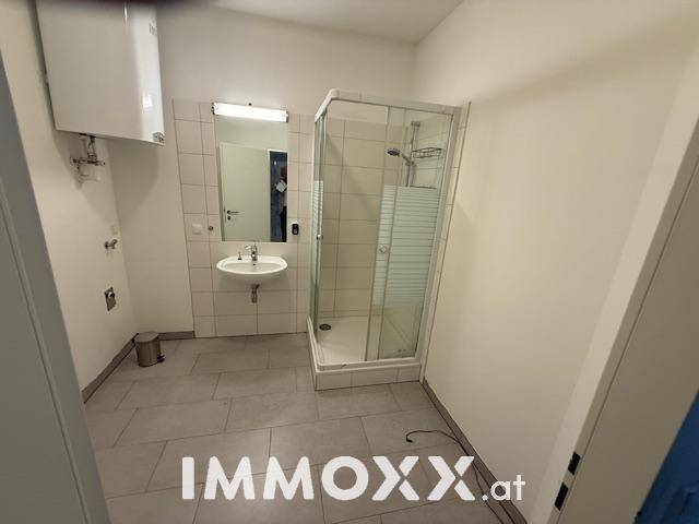 Helles Badezimmer mit Duschkabine, Waschbecken und weißen Wand- und Bodenfliesen.
