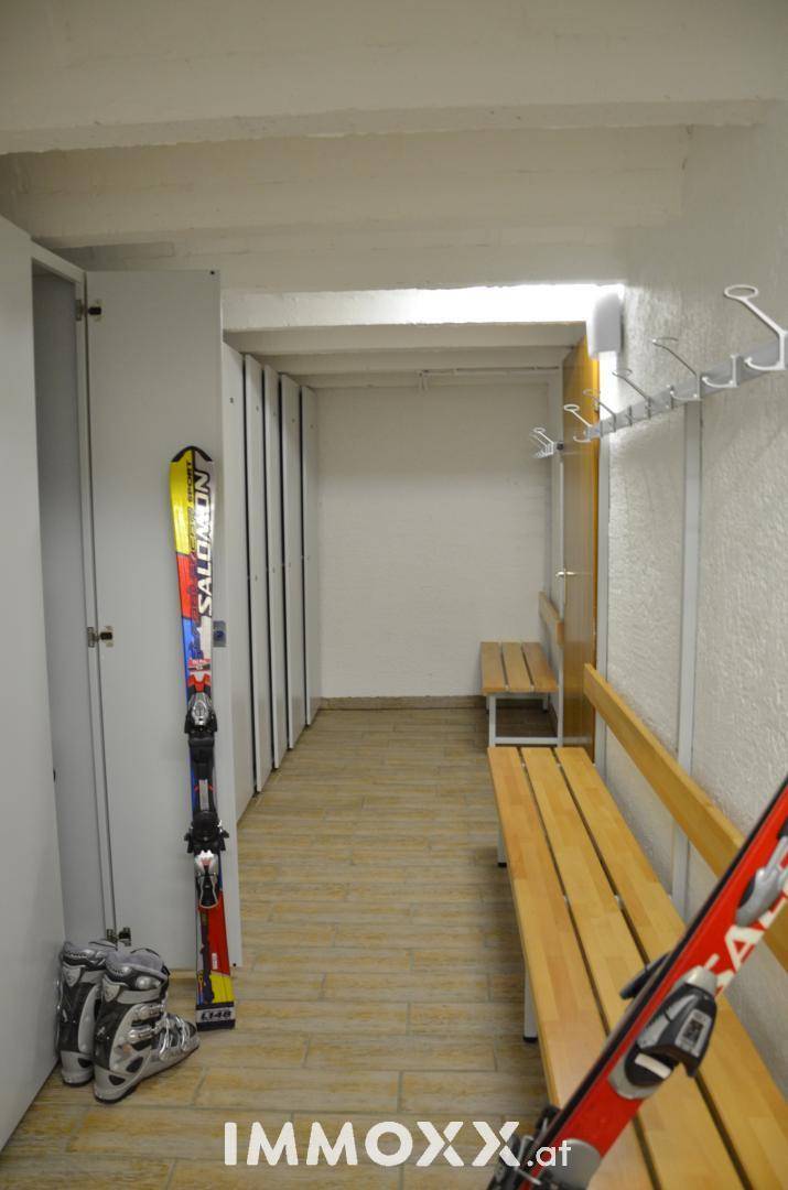 Praktischer Skiraum mit Holzbänken, Garderobenhaken und Schließfächern für Sportausrüstung.