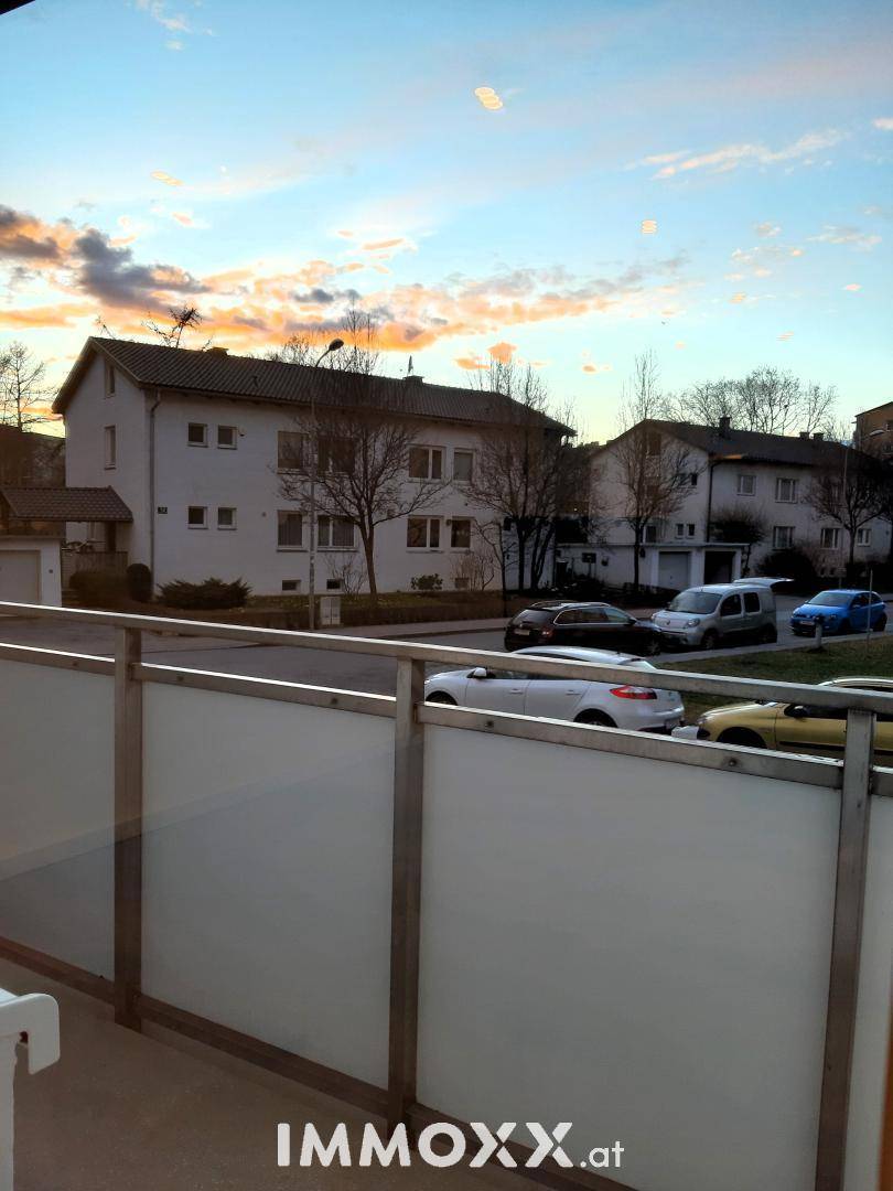 Blick von einem Balkon auf die umliegende Wohngegend bei Sonnenuntergang, mit parkenden Autos.