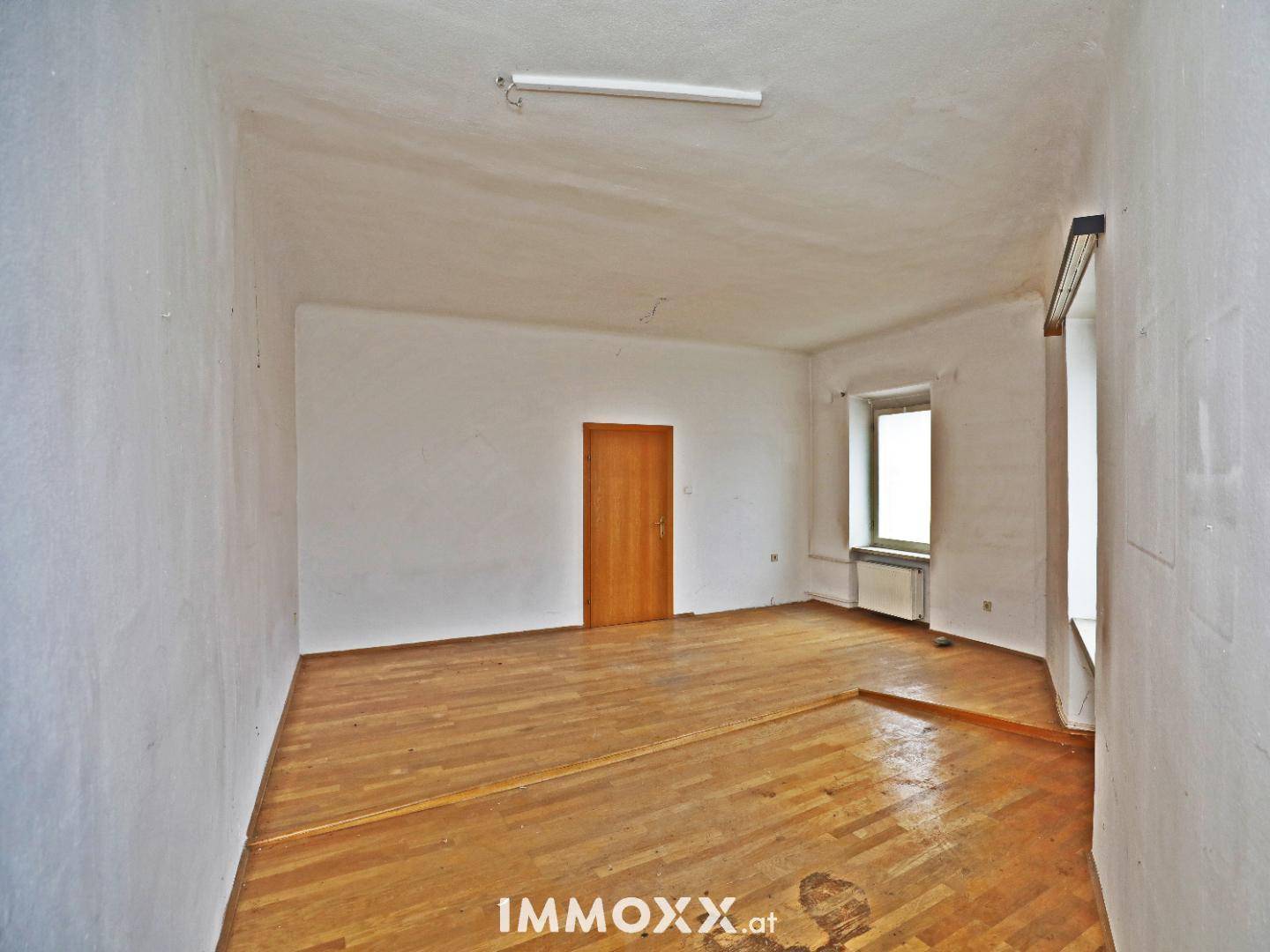 Unmöblierter Raum mit Holzboden und einem Fenster, bereit für eine Modernisierung.