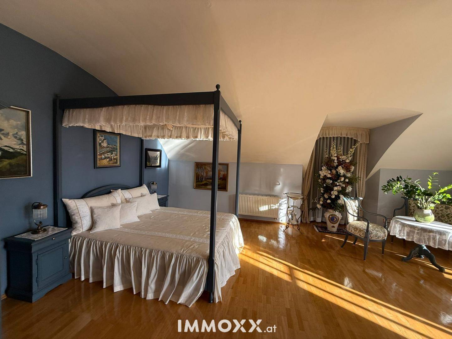 Schlafzimmer mit Himmelbett, blauer Akzentwand, Parkettboden und gemütlichen Dachschrägen.