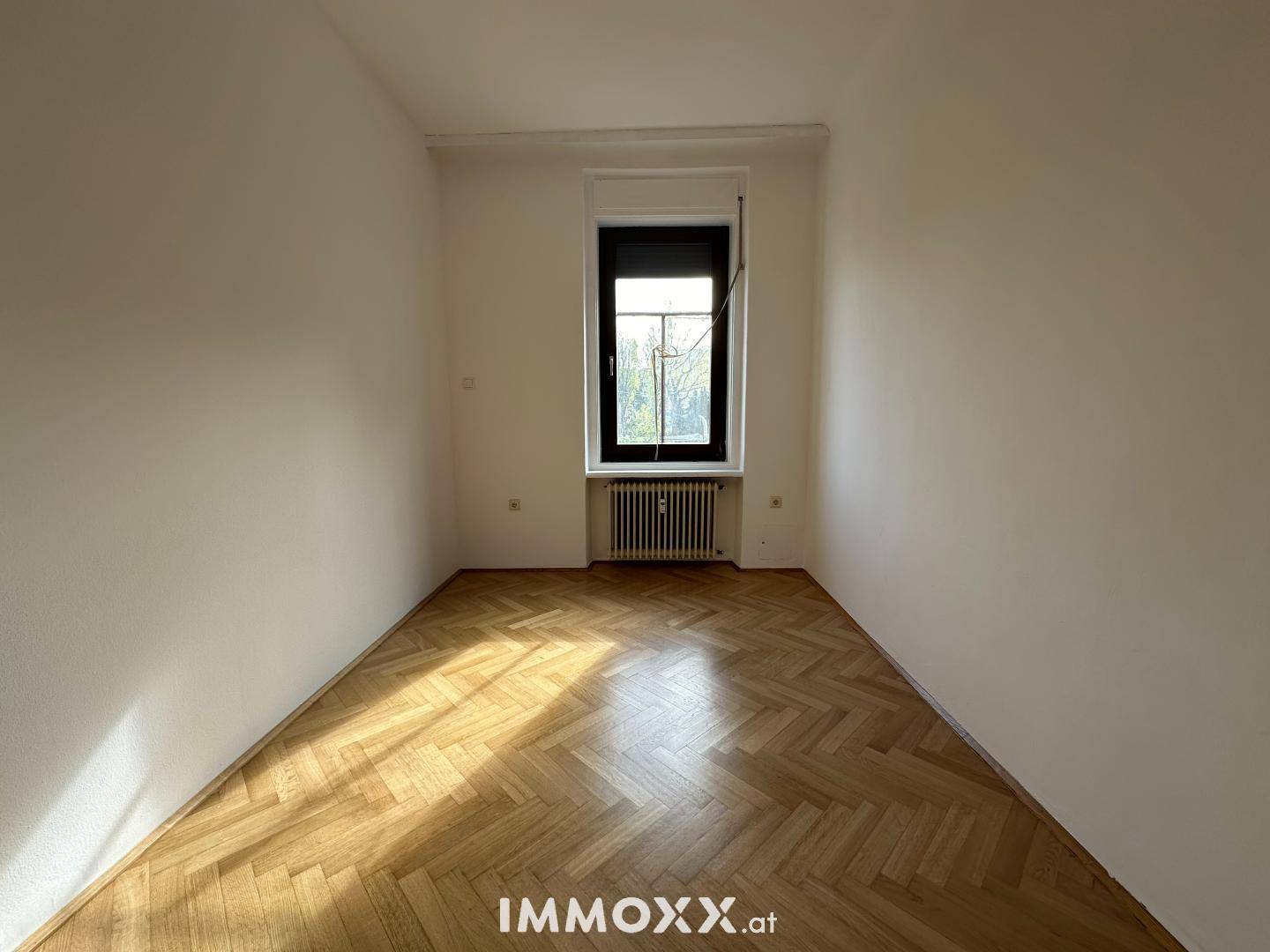 Schmaler Raum mit Fischgrätparkett und einem einzelnen Fenster, das viel Licht hereinlässt.