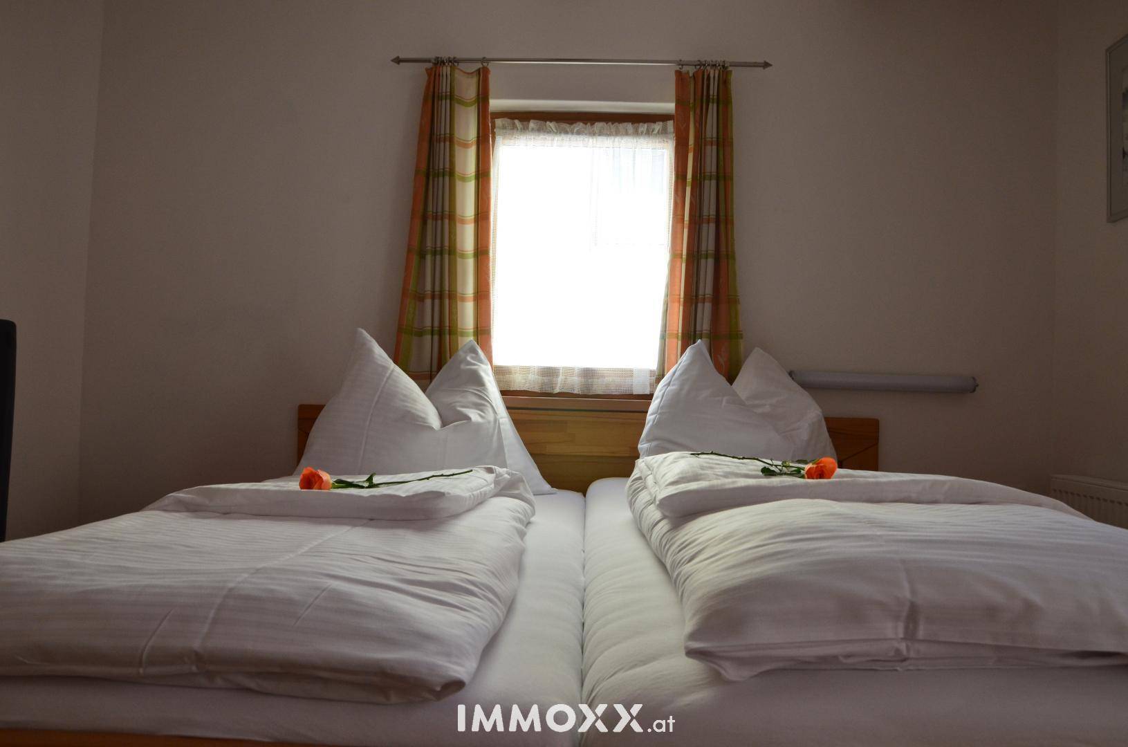 Gemütliches Schlafzimmer mit zwei Einzelbetten, einem Fenster und traditionellen Vorhängen sowie sichtbaren Holzbalken.