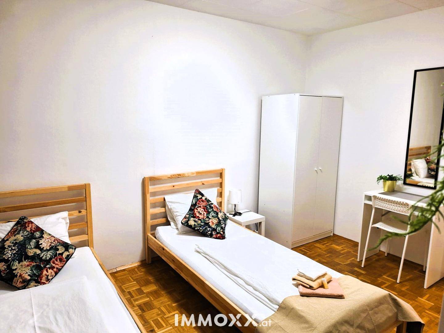 Helles Schlafzimmer mit zwei Einzelbetten, Parkettboden und weißem Kleiderschrank.