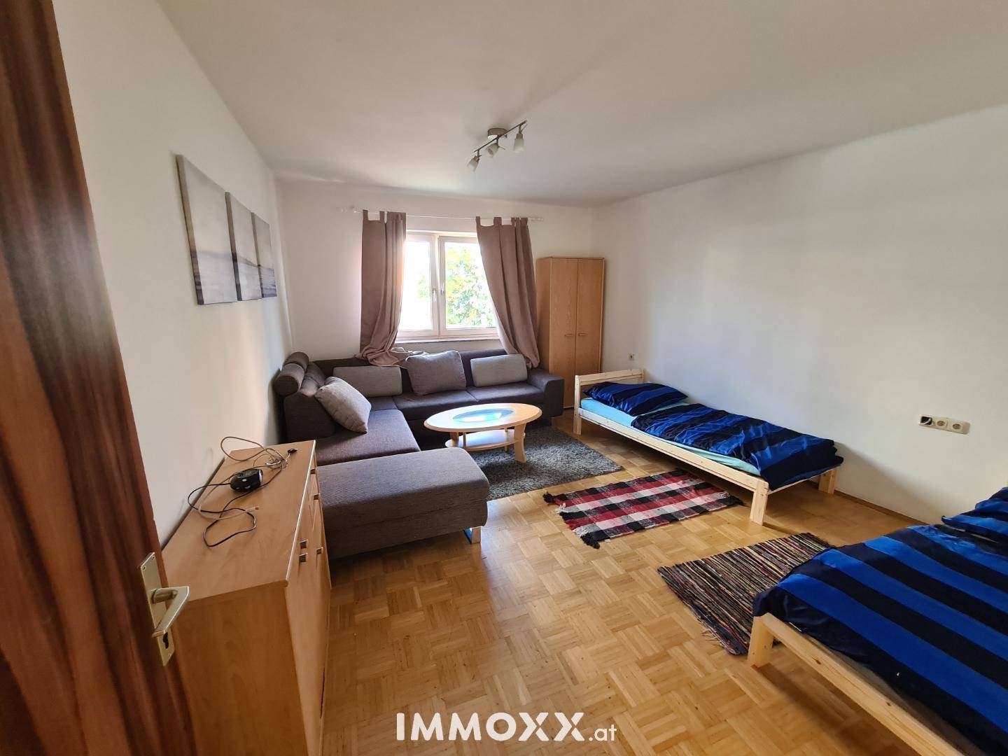 Gemütliches Wohnzimmer mit Sofa, Couchtisch und zwei Einzelbetten, ausgestattet mit Parkettboden.