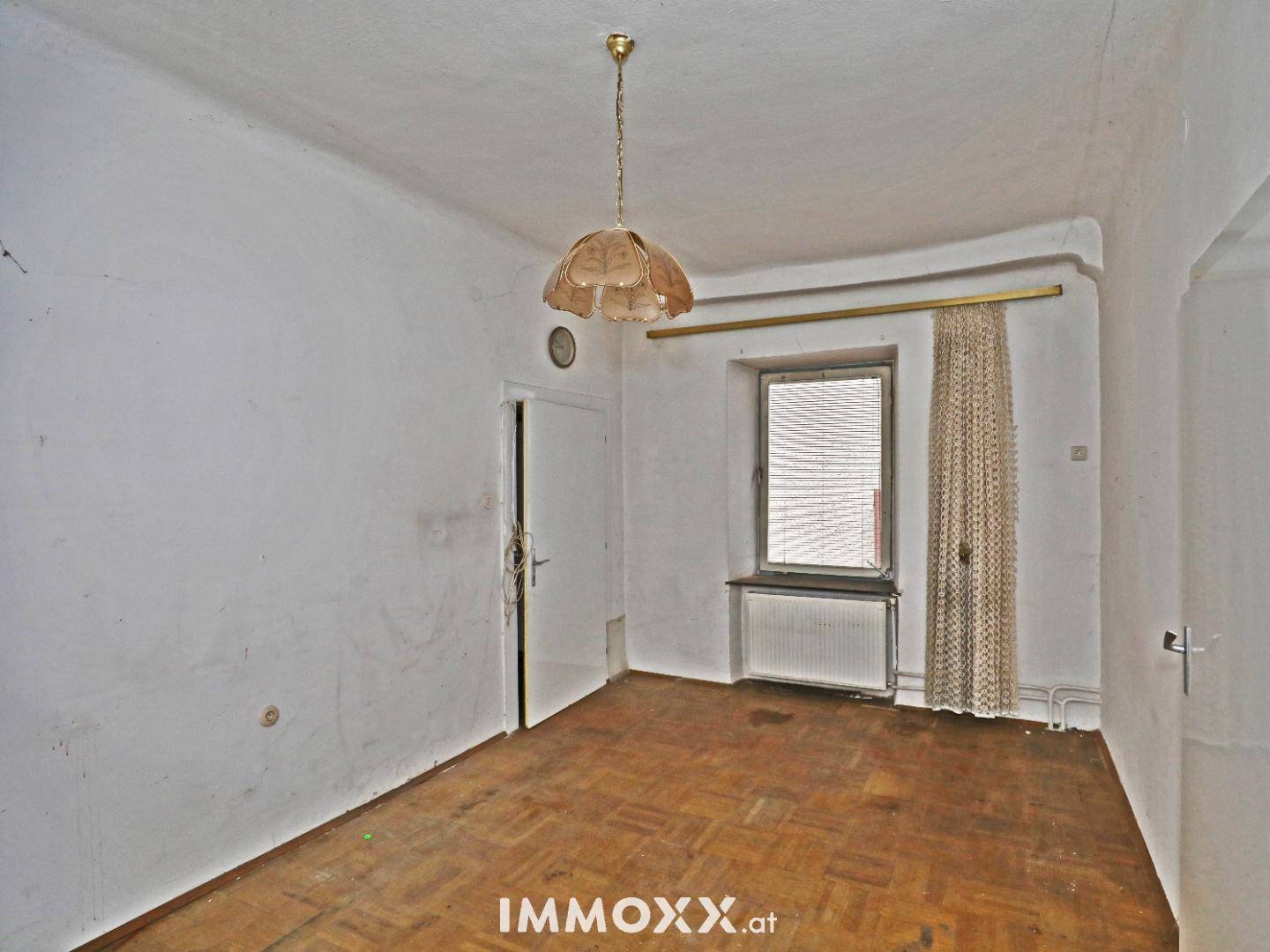 Kleinerer Raum mit Holzboden, Fenster und Vorhang, ideal als Schlaf- oder Gästezimmer.