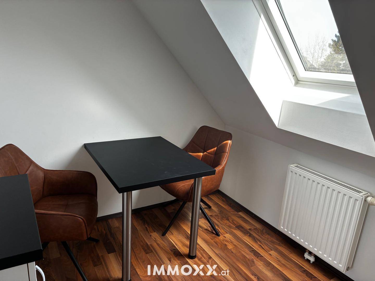 Kleiner Essbereich unter einem Dachfenster mit Tisch, Stühlen und Heizkörper im Dachgeschoss.