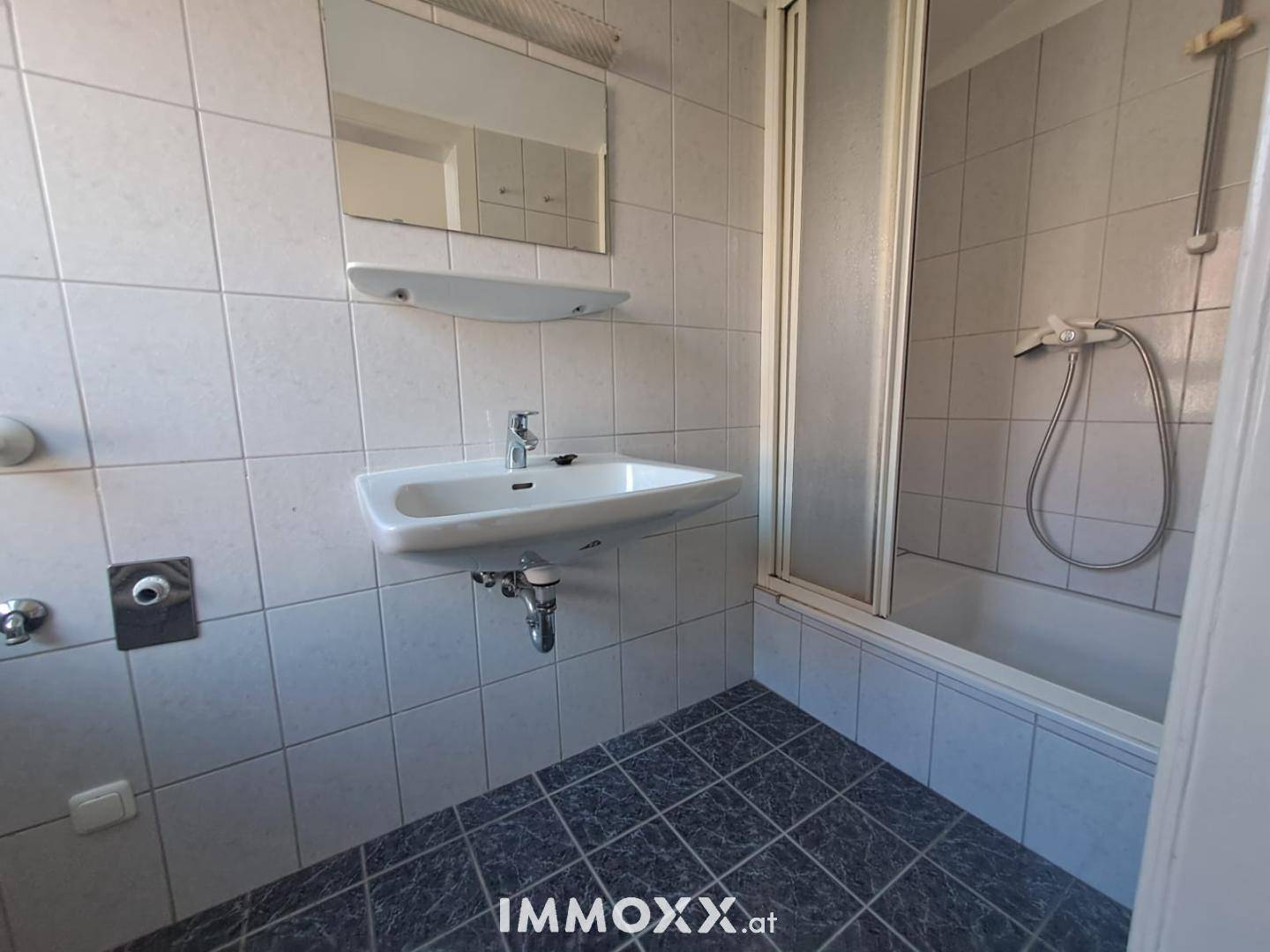 Badezimmer mit Badewanne und integrierter Dusche, Einzelwaschbecken und hellen Wandfliesen.
