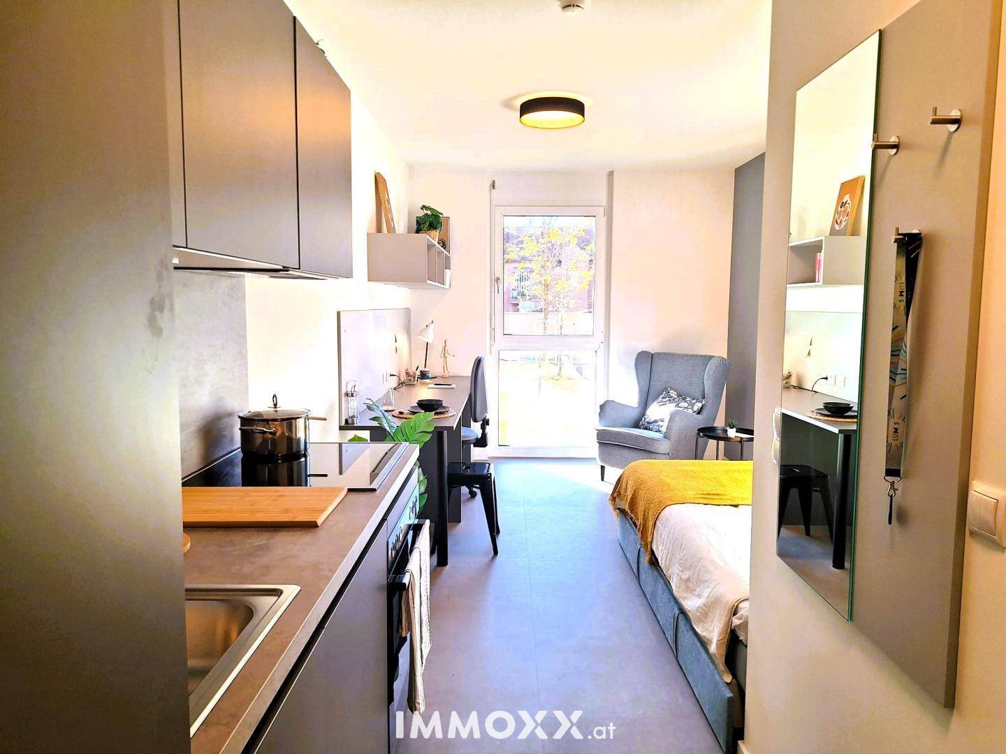 Studio-Apartment mit Küchenzeile, Schlafbereich, Schreibtisch und Sessel für komfortables Wohnen.