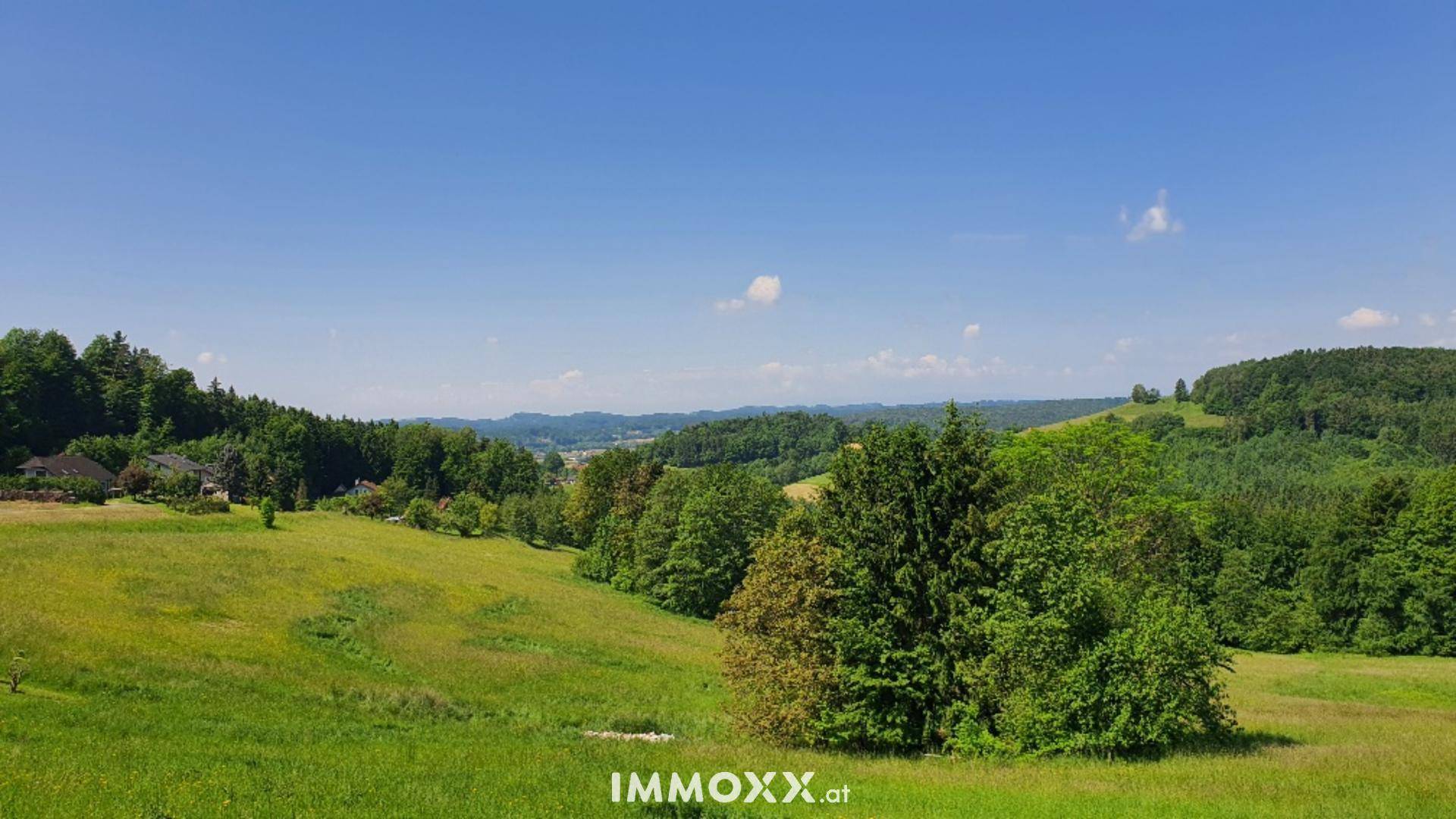 Weitläufige grüne Landschaft mit Wäldern und Hügeln unter blauem Himmel.