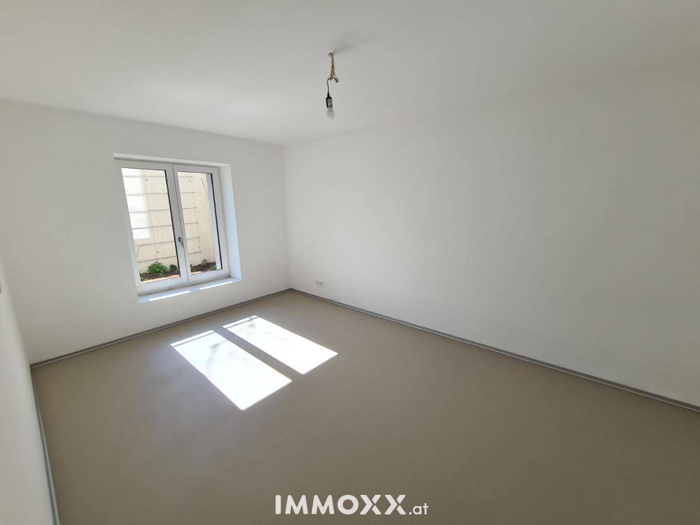 Helles Schlafzimmer mit modernem Bodenbelag und großem Fenster für natürliche Belichtung.