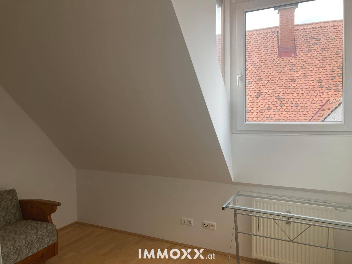 Heller Raum im Dachgeschoss mit schrägen Wänden, Fenster und Heizkörper.
