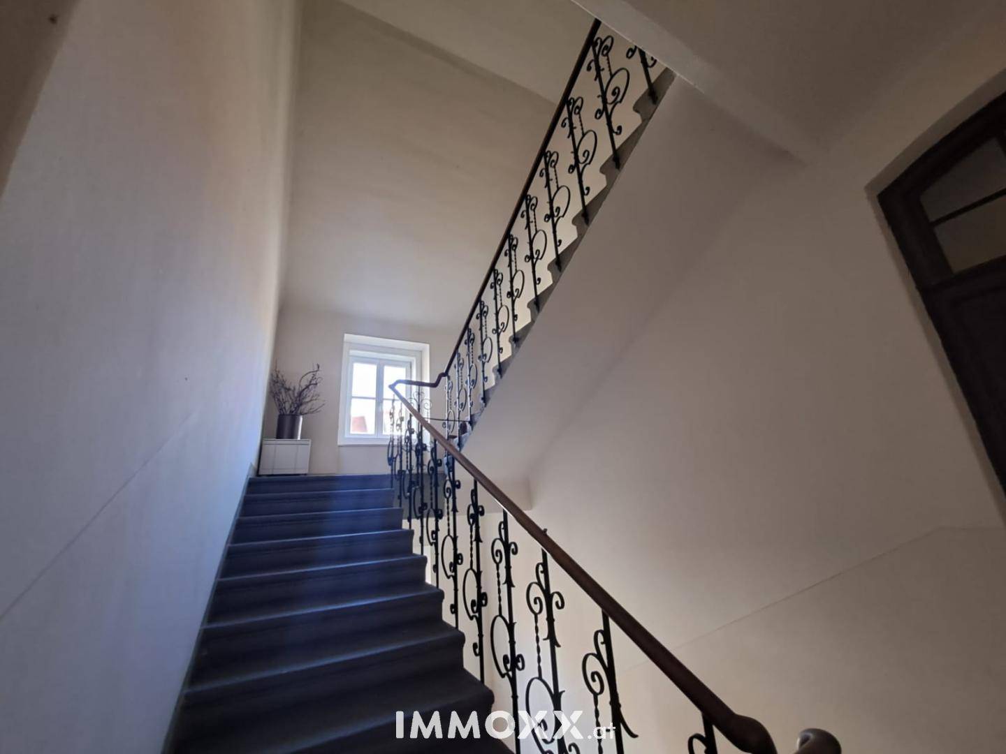 Historisches Treppenhaus mit schmiedeeisernem Geländer und hohen Wänden in einem Altbau.