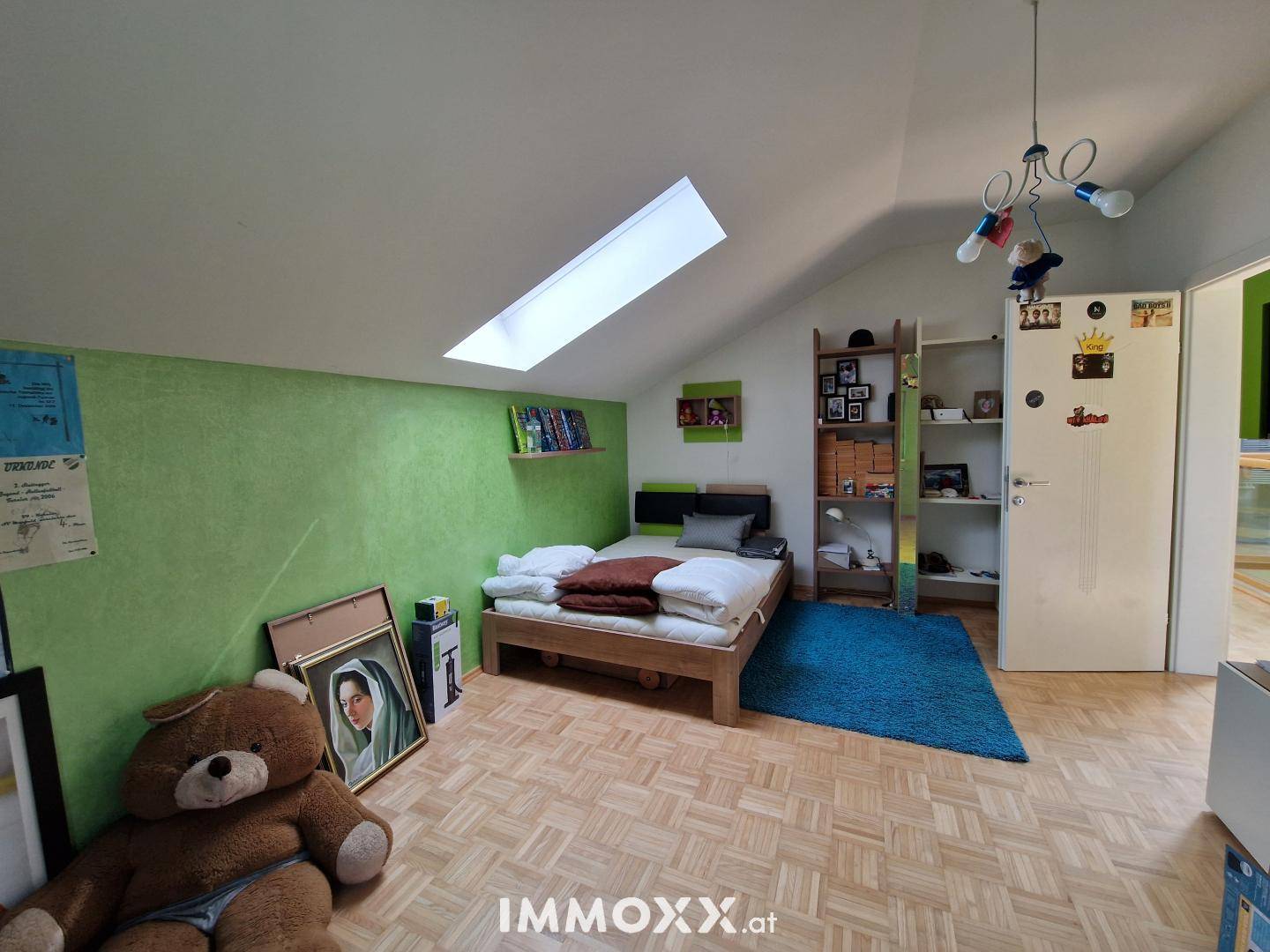 Kinderzimmer oder Gästezimmer mit grüner Akzentwand, Holzbett, Parkettboden und Dachfenster.
