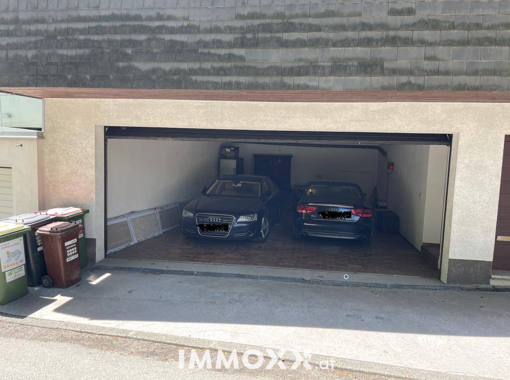 Doppelgarage mit zwei geparkten Fahrzeugen und Mülltonnen im Außenbereich.